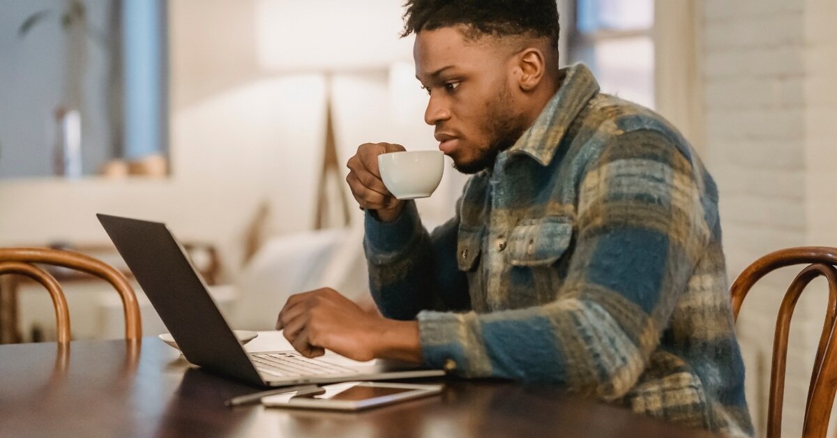 Young South African drinking coffee while working on his laptop at home to make a passive income