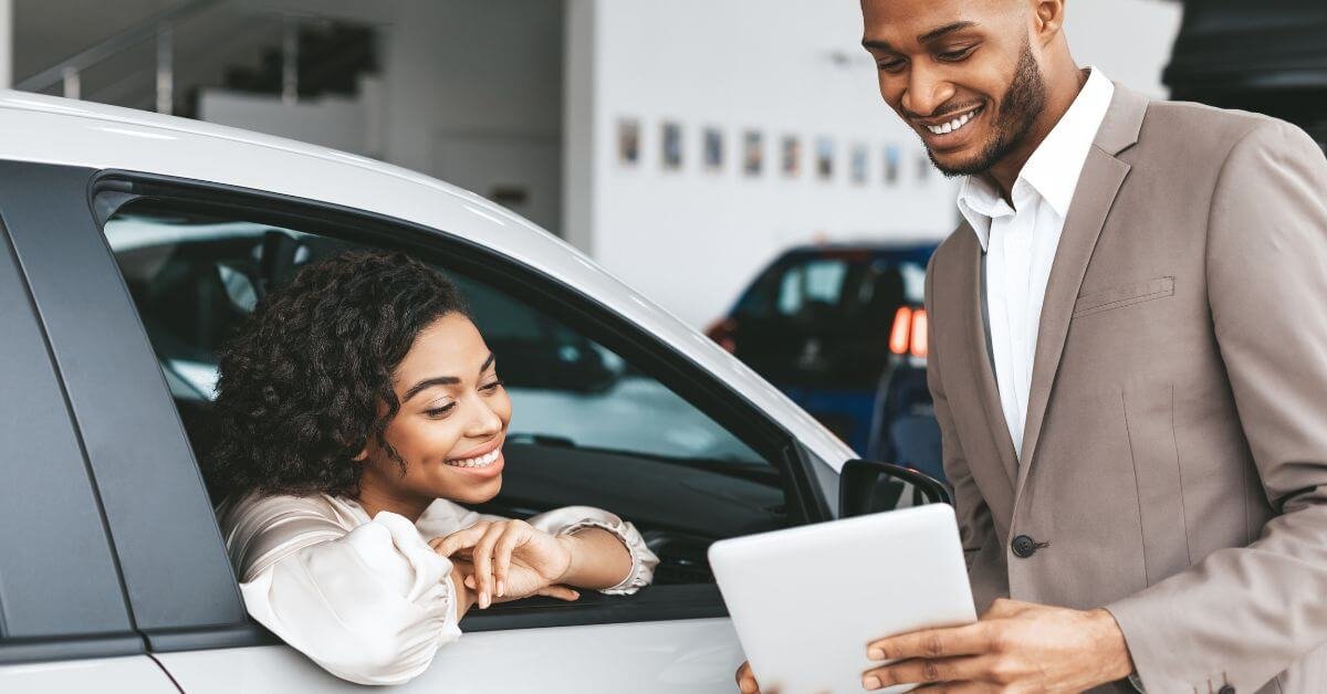 Young woman sitting in a new car while car salesman shows her a tablet