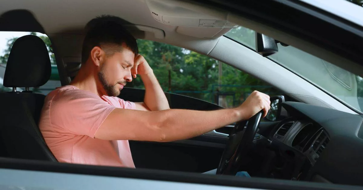 Stressed man in pink shirt resting head on hand while sitting in car.