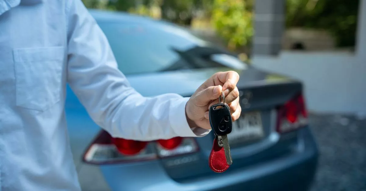Person in a white shirt holding car keys with a blue car in the background