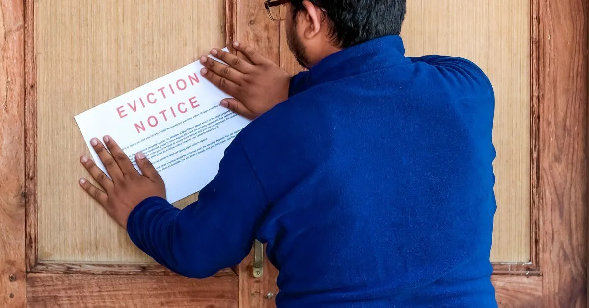 A man wearing a blue shirt posting an eviction notice on a wooden door.