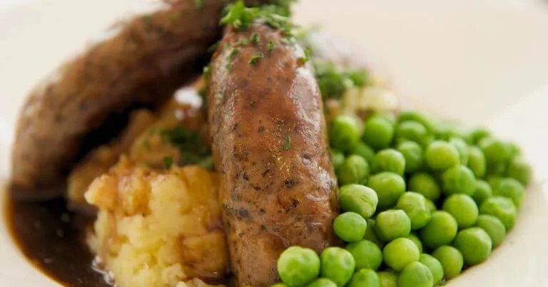 
Sausages with mashed potatoes, peas, and gravy on a plate.