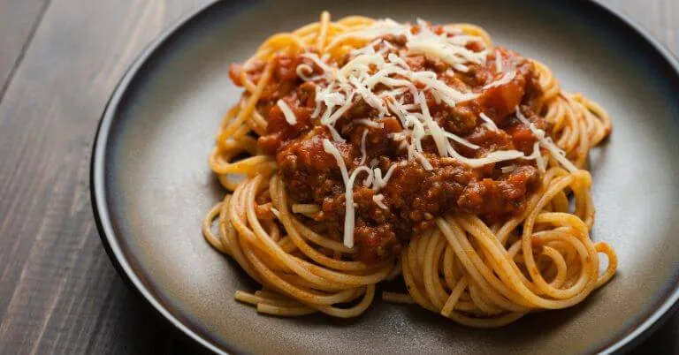 Spaghetti bolognese with meat sauce and shredded cheese on a dark plate.