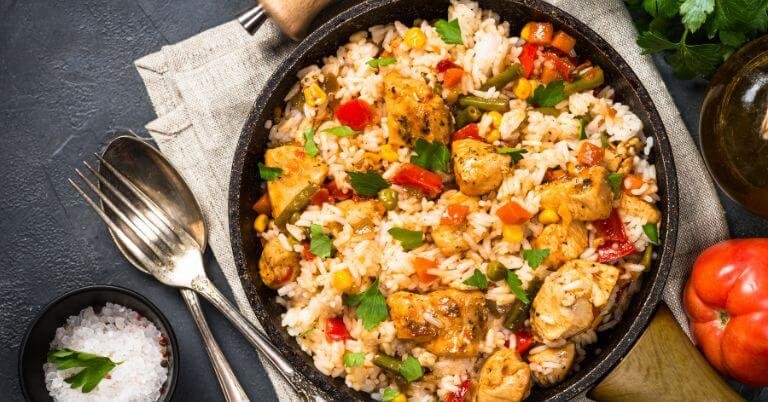 Chicken and vegetable rice in a skillet, with herbs on the side.