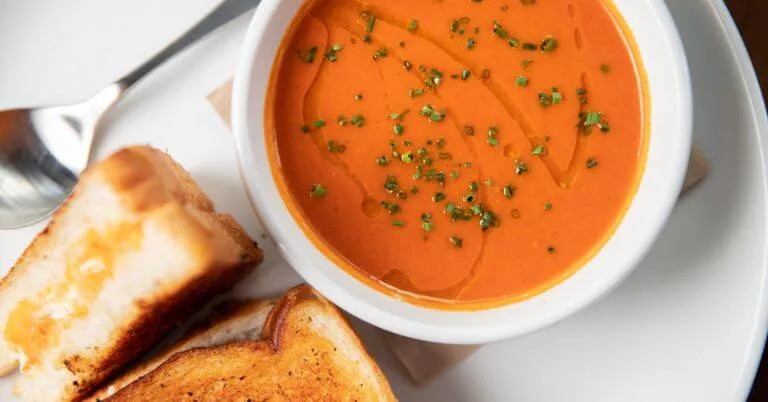 Tomato soup with chives and grilled cheese sandwiches on the side.