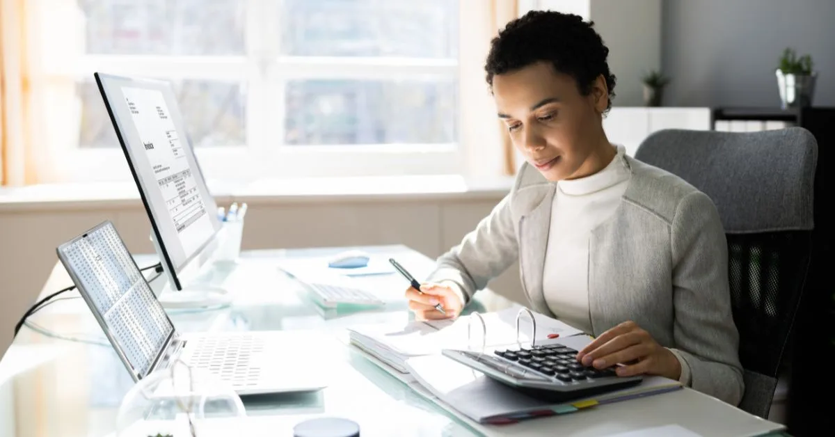 Professional accountant using a calculator and reviewing financial documents in a bright office.