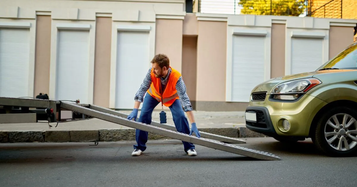 Worker in an orange safety vest setting up a ramp to repossess car with a tow truck